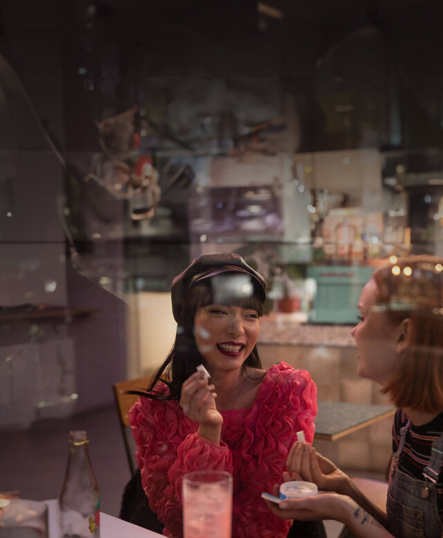 Two women sitting at bar table. They are holding ZYN nicotine pouches and a ZYN can in their hands.
