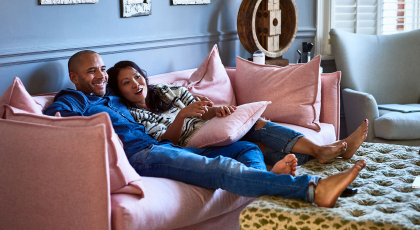 A man and a woman sitting on a pink couch in the living room