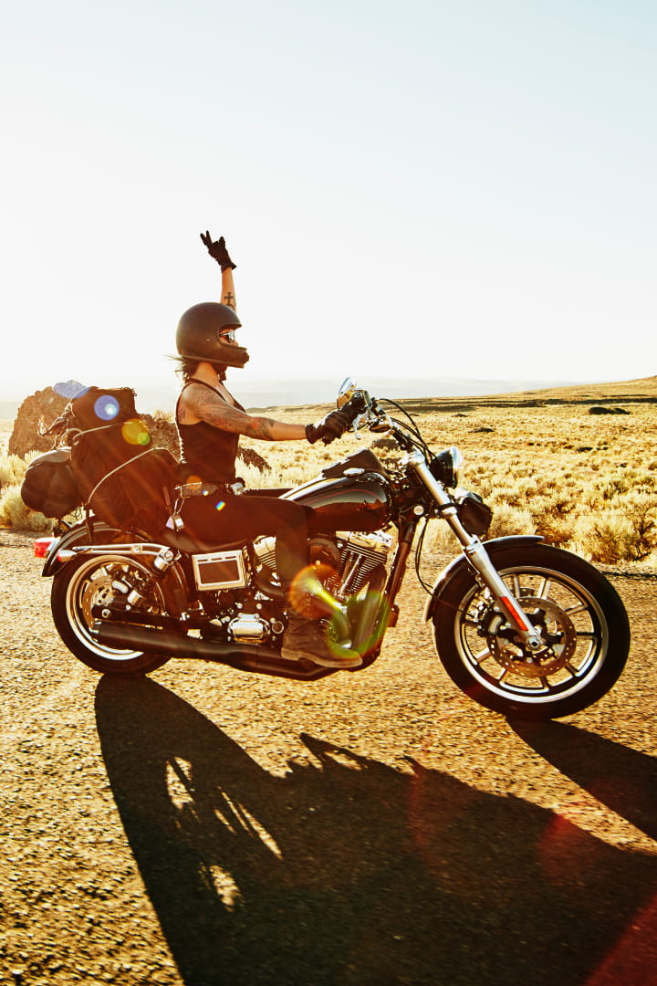 A woman on a motorbike on the road with a raised hand