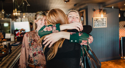Two women hugging and a third women looking at them and smiling